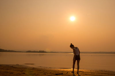 Rear view of woman standing at beach during sunset