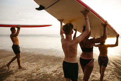 Family carrying paddleboards on heads while walking at beach during vacation