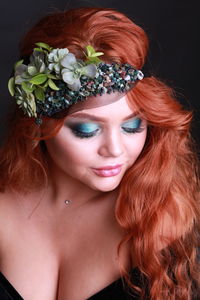 Close-up of sensuous young woman wearing wreath against black background