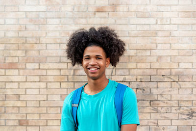 Afro latin male teenager smiling against a wall