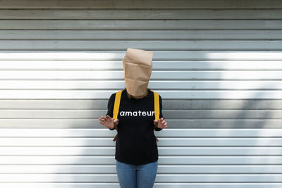 Woman covering face with paper bag while standing against shutter
