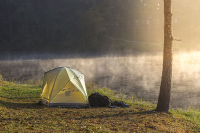 Tent on riverbank by lake in forest