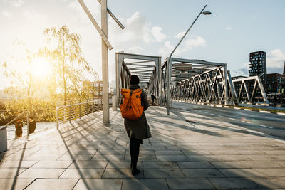 Rear view of woman carrying backpack while walking on bridge