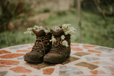 High angle of brown worn boots on table with soft white flowers inside and green garden on blurred background