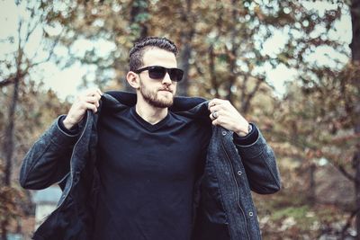 Handsome man wearing jacket while standing against trees in yard