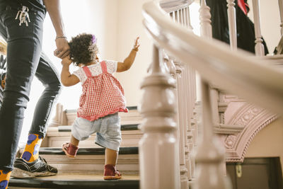 Baby girl holding hand of father while climbing steps in apartment