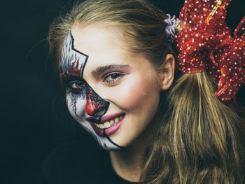 Close-up portrait of smiling woman with painted face against black background