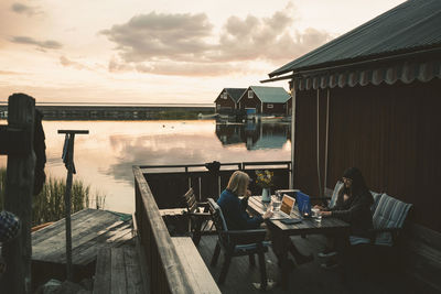 Friends using laptop at table in holiday villa by lake against sky