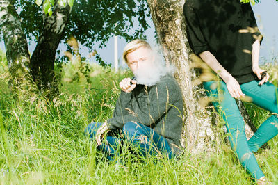 Friends smoking by tree on field