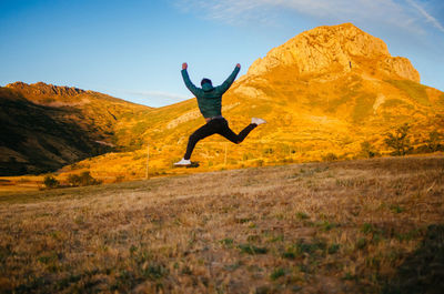 Back view of unrecognizable male in casual clothes jumping high against mountains