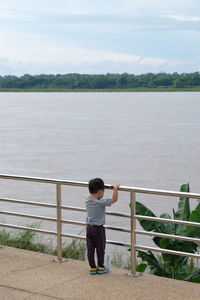 Rear view of boy standing by railing against sea