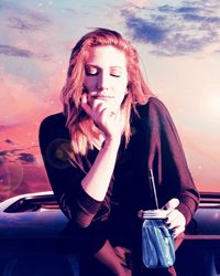 Young woman holding drink on car roof against sky