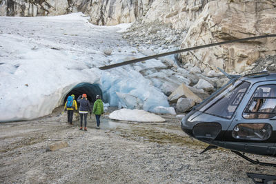 A mountain guide approaches a glacial ice cave with tour clients.