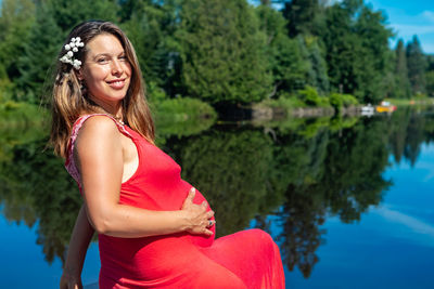 Happy woman standing by lake against trees