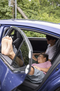 Smiling boy resting on brother's lap with feet up on car door