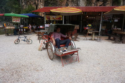 Man sitting in pedicab by sidewalk cafe in city