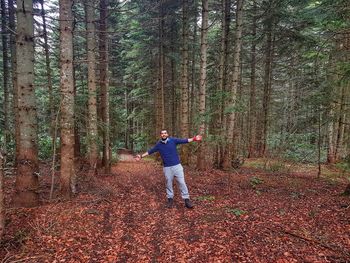 Full length of man with arms outstretched standing by trees in forest