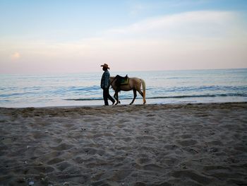 Man riding horse on beach against sky