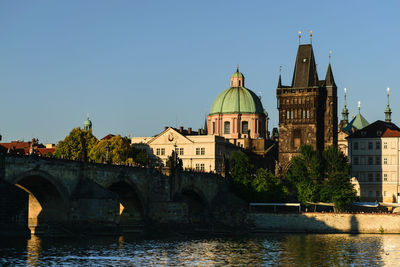 Arch bridge over river by buildings against clear sky