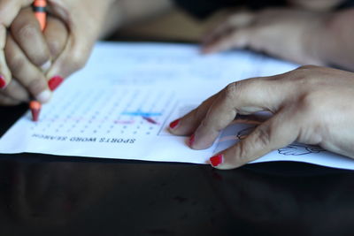 Cropped hands of girl with mother writing on paper at table