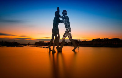 Silhouette couple and woman against sky during sunset