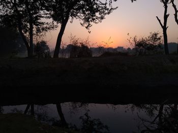 Silhouette trees by lake against sky during sunset