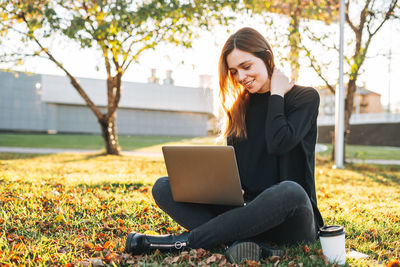 Young woman using laptop while sitting on field