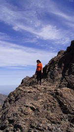 Low angle view of woman standing on rocky mountains against sky