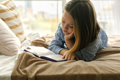 Young woman using mobile phone while lying on bed at home