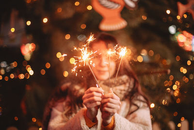Teenage girl holding sparklers standing by luminous christmas tree
