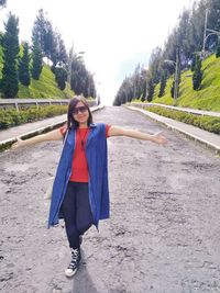 Full length portrait of young woman standing against trees