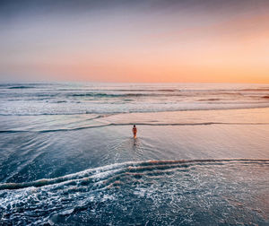 Woman wading in sea against sky during sunset
