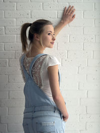 Rear view of thoughtful woman looking away while standing against wall