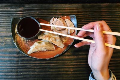 Cropped image of woman hand holding chopsticks over plate with food