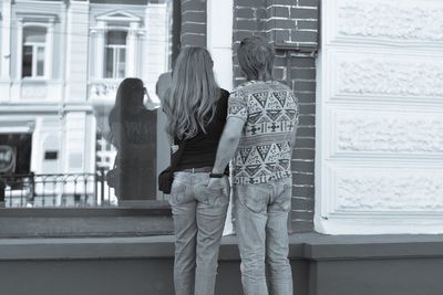 Rear view of two women standing against window