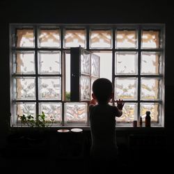 Rear view of boy standing by window at home