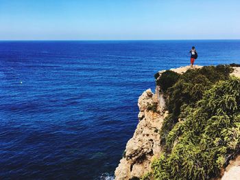 Man standing on cliff by sea against clear sky