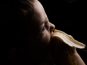 Close-up of boy eating banana in darkroom