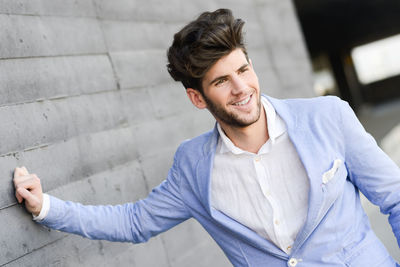 Young man smiling while standing by wall