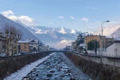 Snow covered houses by buildings against sky during winter