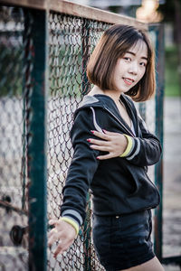 Portrait of woman standing by chainlink fence