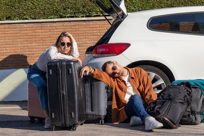 Young couple sleeping on the floor near their car with all the siutcases wating someone 