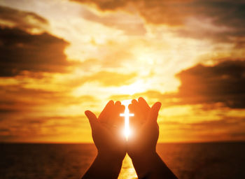 Digital composite image of silhouette hand holding sunlight cross against sky