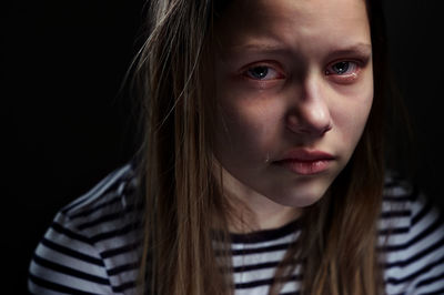 Close-up portrait of sad young woman against black background