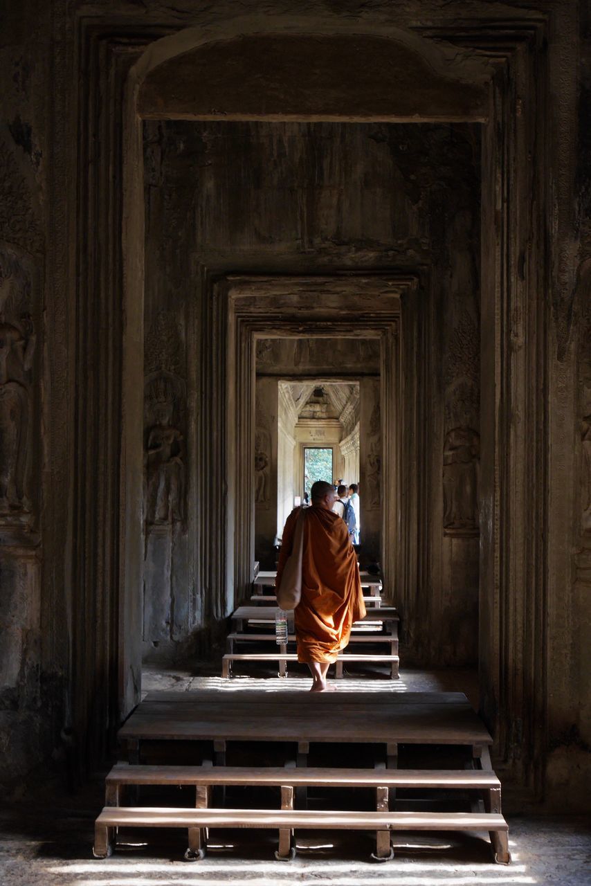 architecture, religion, one person, spirituality, belief, temple, adult, built structure, temple - building, rear view, building, history, monk, indoors, the past, place of worship, travel destinations, praying, men, sitting, clothing, ancient history, statue, full length, person, travel, light, lifestyles, robe, relaxation, ancient