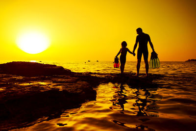 Silhouette people on beach against sky during sunset