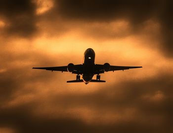 Low angle view of silhouette airplane flying against sky at sunset