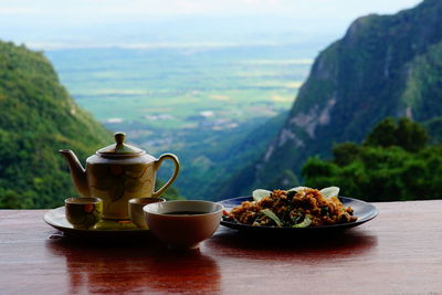 Close-up of tea and food on table against mountains