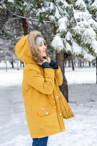 Side view of young woman in warm clothing standing at snow covered forest