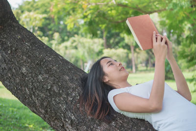 Young woman using phone while sitting on tree trunk